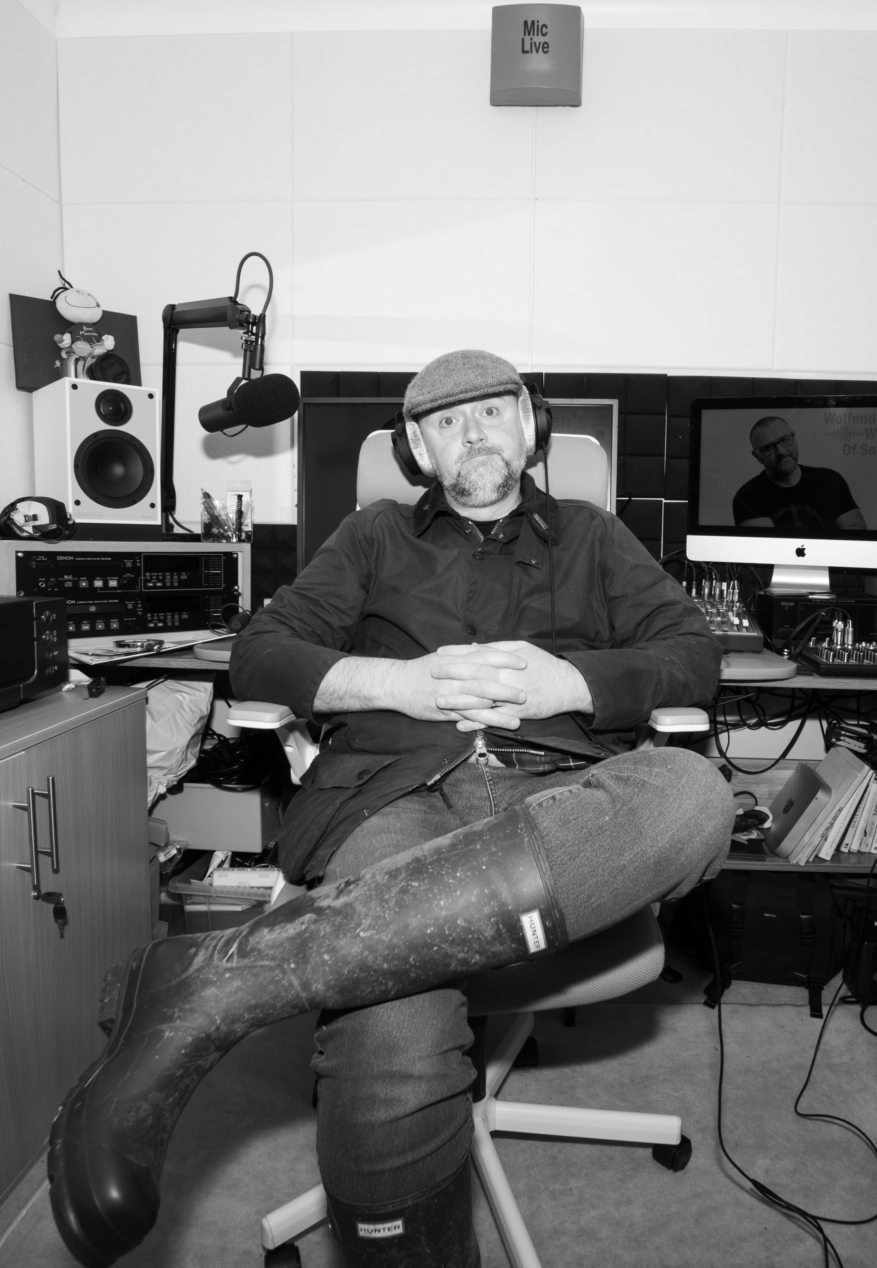 A photo of Martin in his podcast studio dressed in a barbour jacket, green wellies and a flat cap. He also has headphones on. This was taken for an episode of a podcast relating to the countryside. 